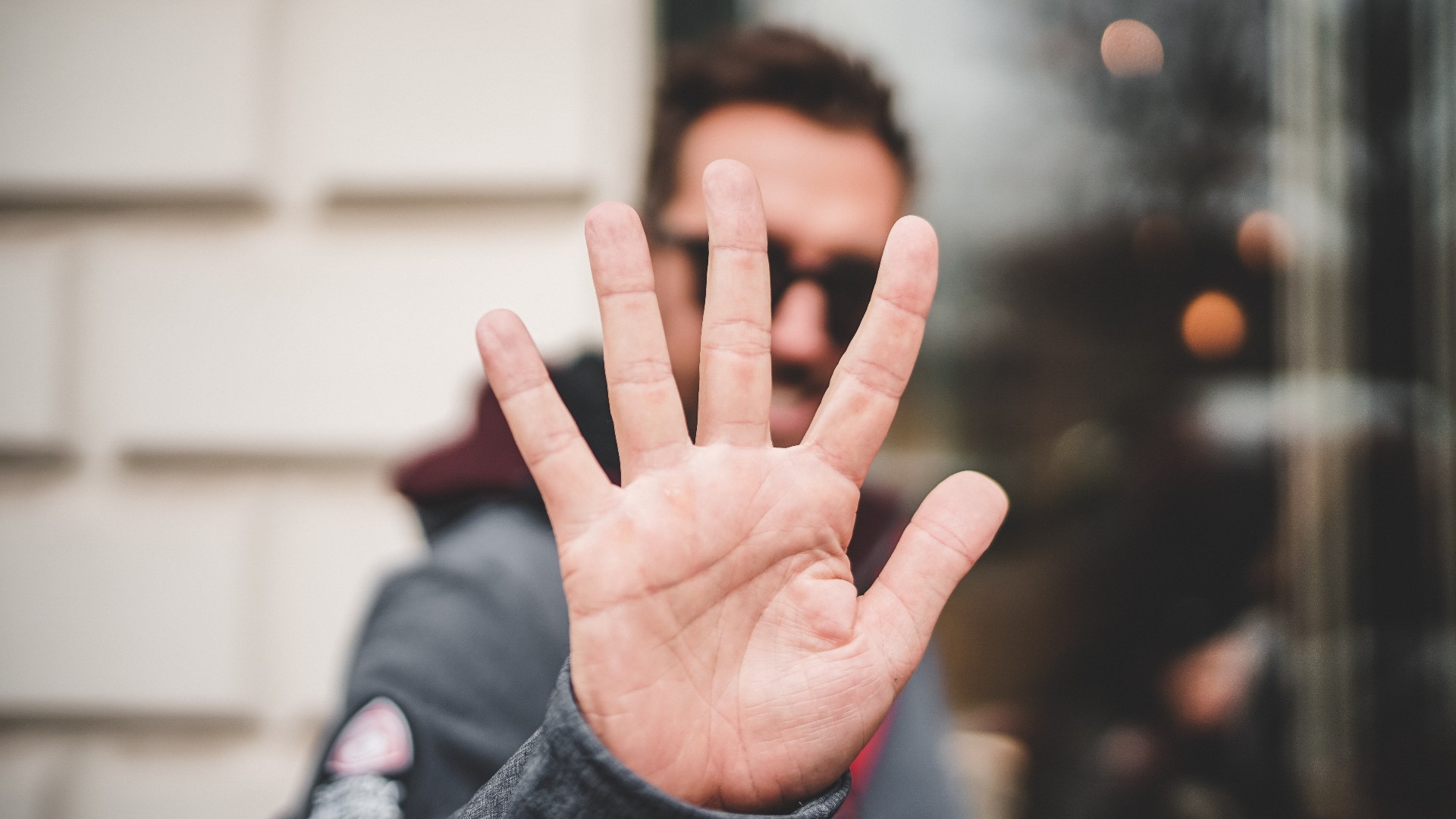 A man holding up five fingers, obscuring his face